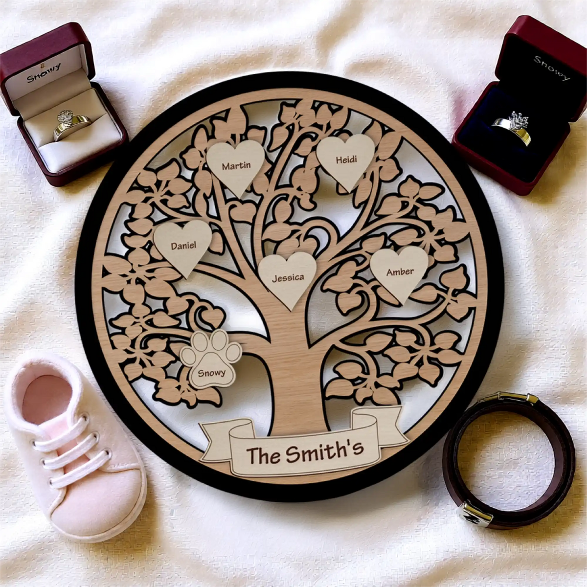 Wooden family tree with personalized names, surrounded by jewelry and a baby shoe, on a light background.