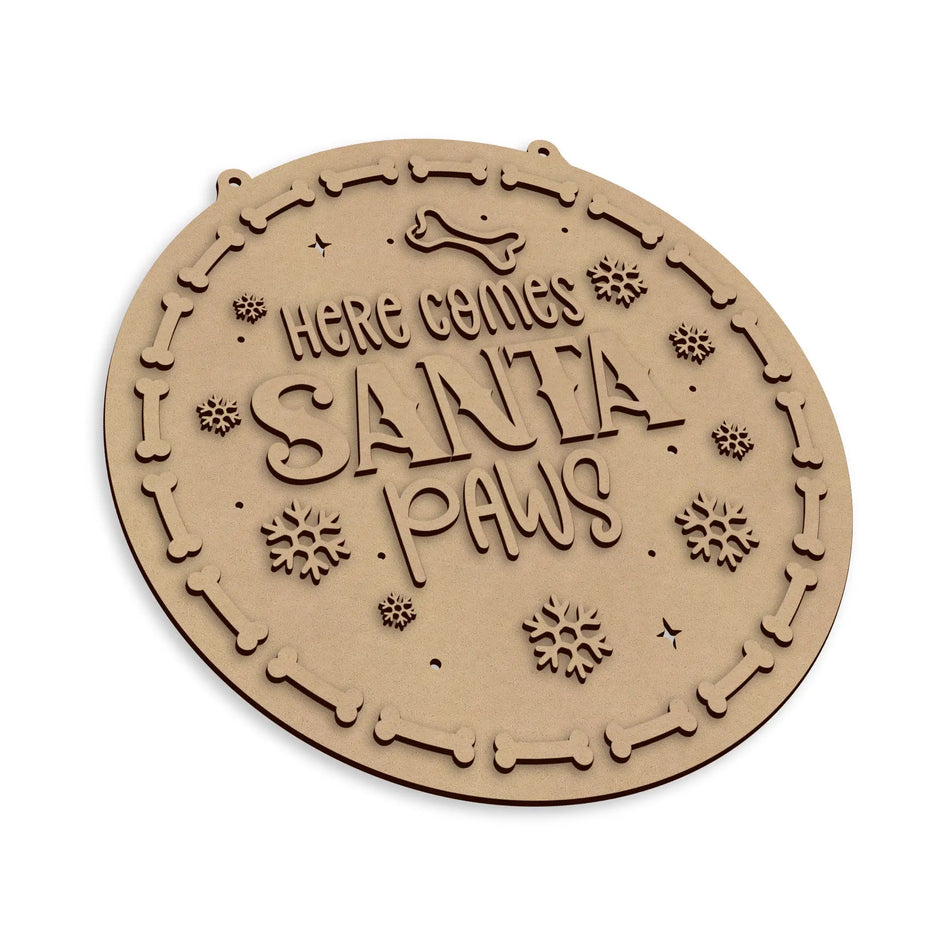 A round, laser-cut wooden plaque with the text 'HERE COMES SANTA PAWS' and decorative bone border, shown on a plain white background.
