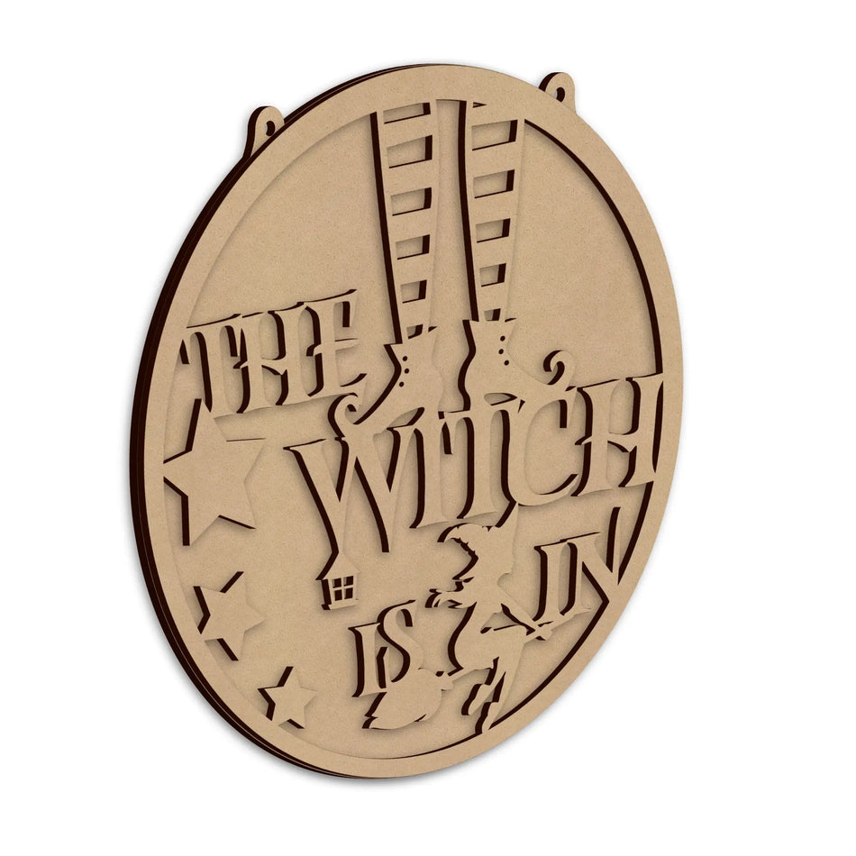 An round-shaped laser-cut wooden wall plaque featuring the phrase 'THE WITCH IS IN', shown on a plain white background.